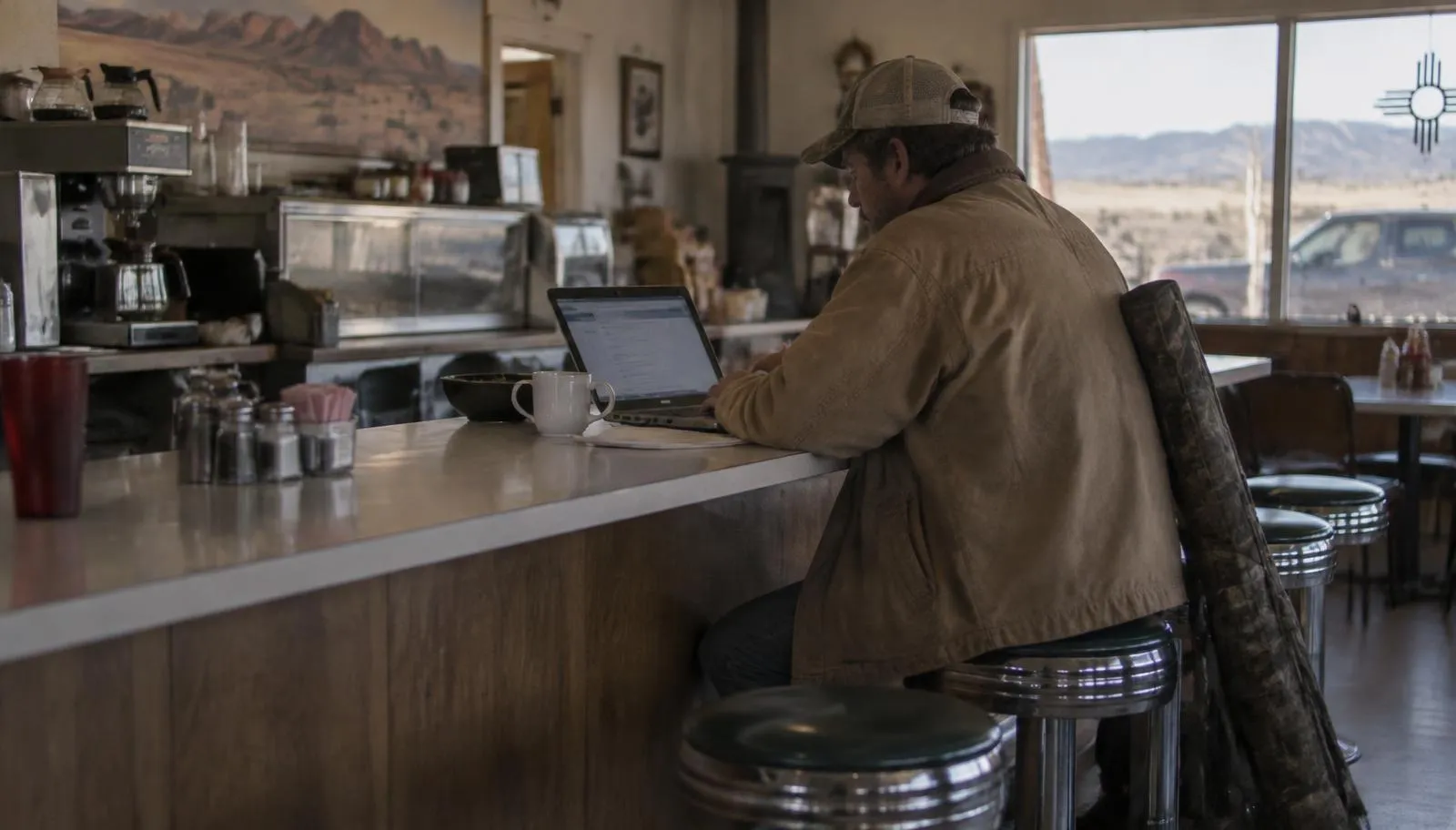 Hunter in a canvas jacket filling out an online license application at a small-town New Mexico diner